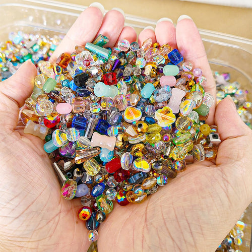 Hands holding a pile of assorted colorful glass beads for jewelry making and crafts. Beads vary in size, shape, and color.
