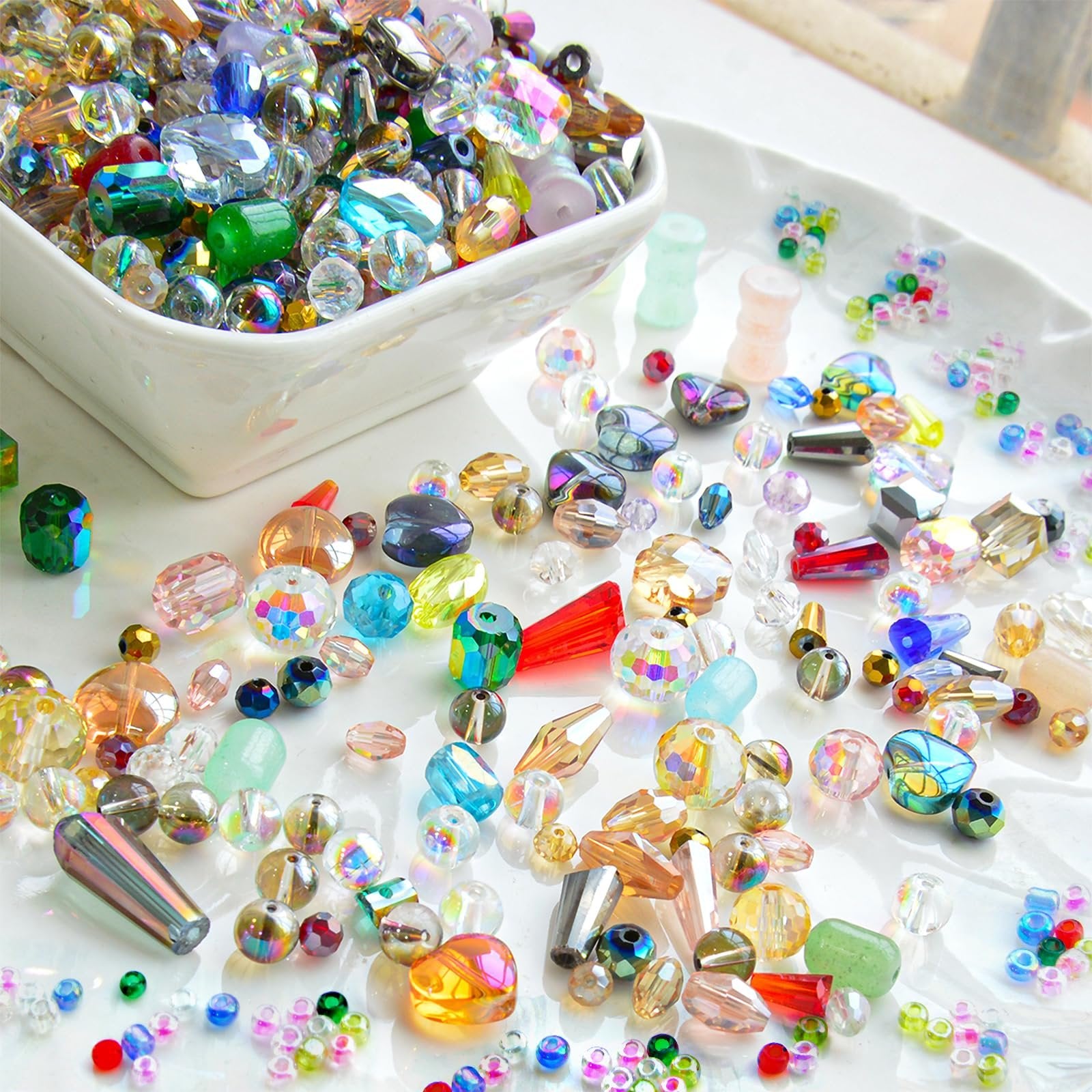 Assorted glass beads in various shapes, sizes, and colors spilling from a white bowl onto a white tray.