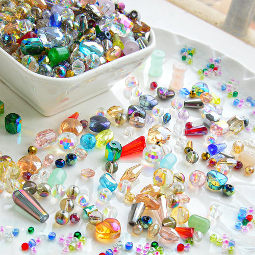 Assorted glass beads in various shapes, sizes, and colors spilling from a white bowl onto a white tray.