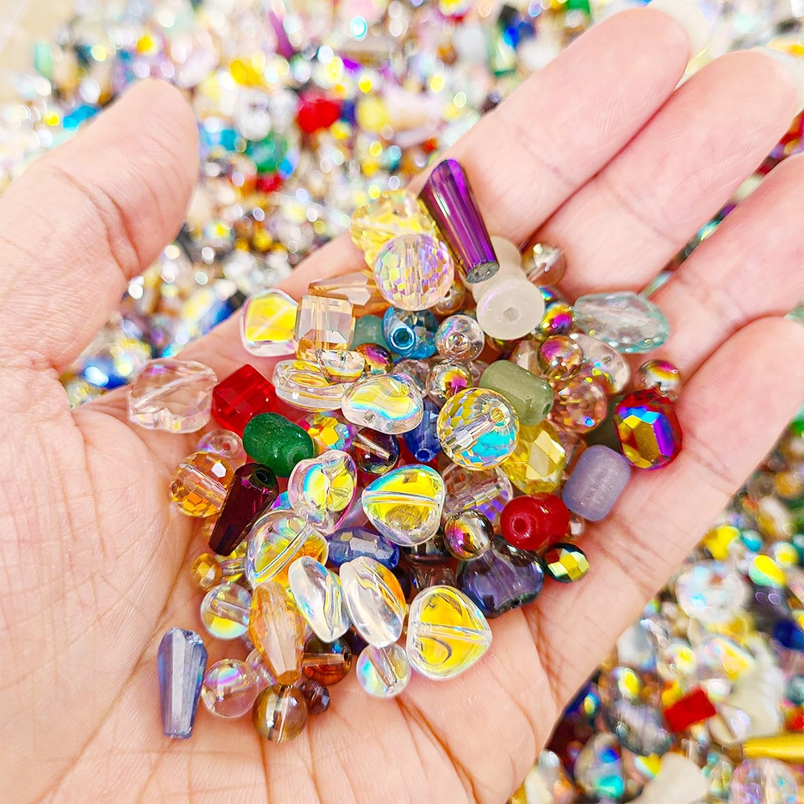 Hand holding assorted colorful glass beads for jewelry making and crafts. Beads vary in size, shape, and color, with some faceted and iridescent finishes.