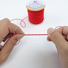 Hands holding a length of red nylon string, with a spool of red nylon string in the background.
