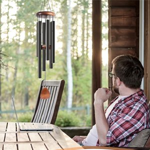 Man sitting on a porch looking at a wind chime hanging outdoors, with a laptop on the table.