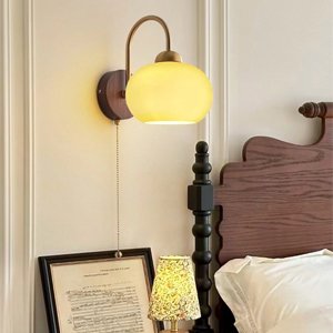 Wall lamp with a curved brass arm and a frosted glass shade, mounted next to a wooden headboard.
