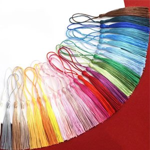 Assortment of colorful nylon tassels with loops for jewelry making, laid out on a red surface.