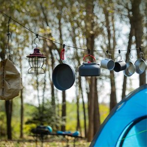 Camping gear including a lantern, frying pan, kettle, and mugs hanging on a line near a tent.