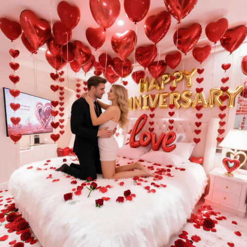 Couple embracing on a bed decorated with red rose petals, heart balloons, and gold anniversary balloons.
