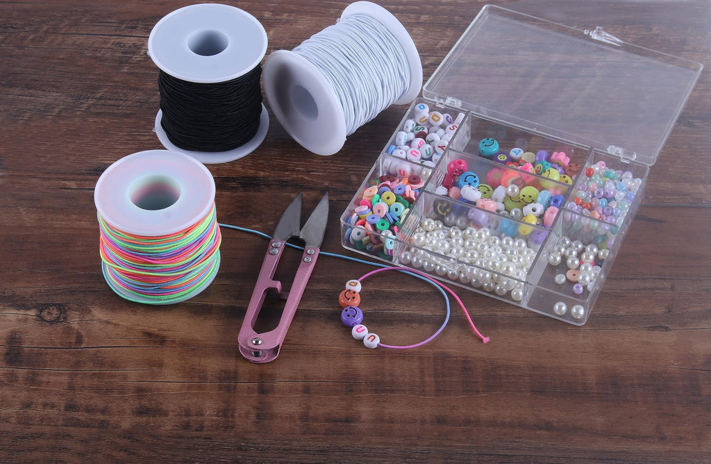Spools of elastic cord, a bead organizer filled with colorful beads, and pink scissors on a wooden surface.