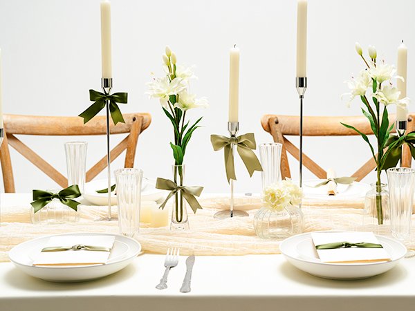 Table setting with candles, flowers, and place settings decorated with green ribbon