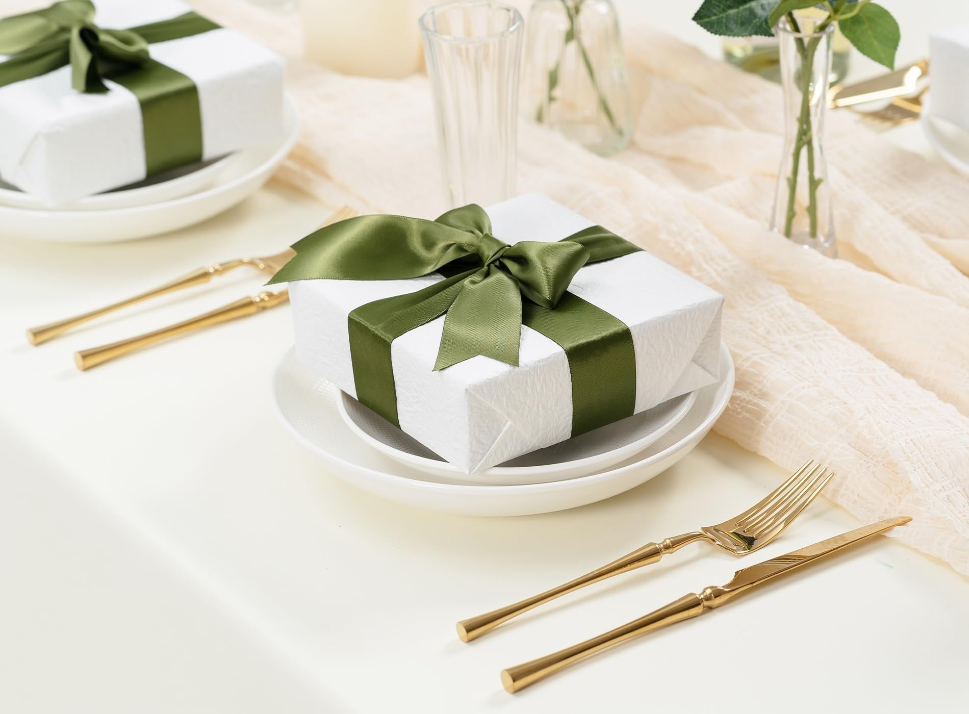 Table setting with a white gift box wrapped in green satin ribbon and a bow, gold cutlery, and decorative elements.