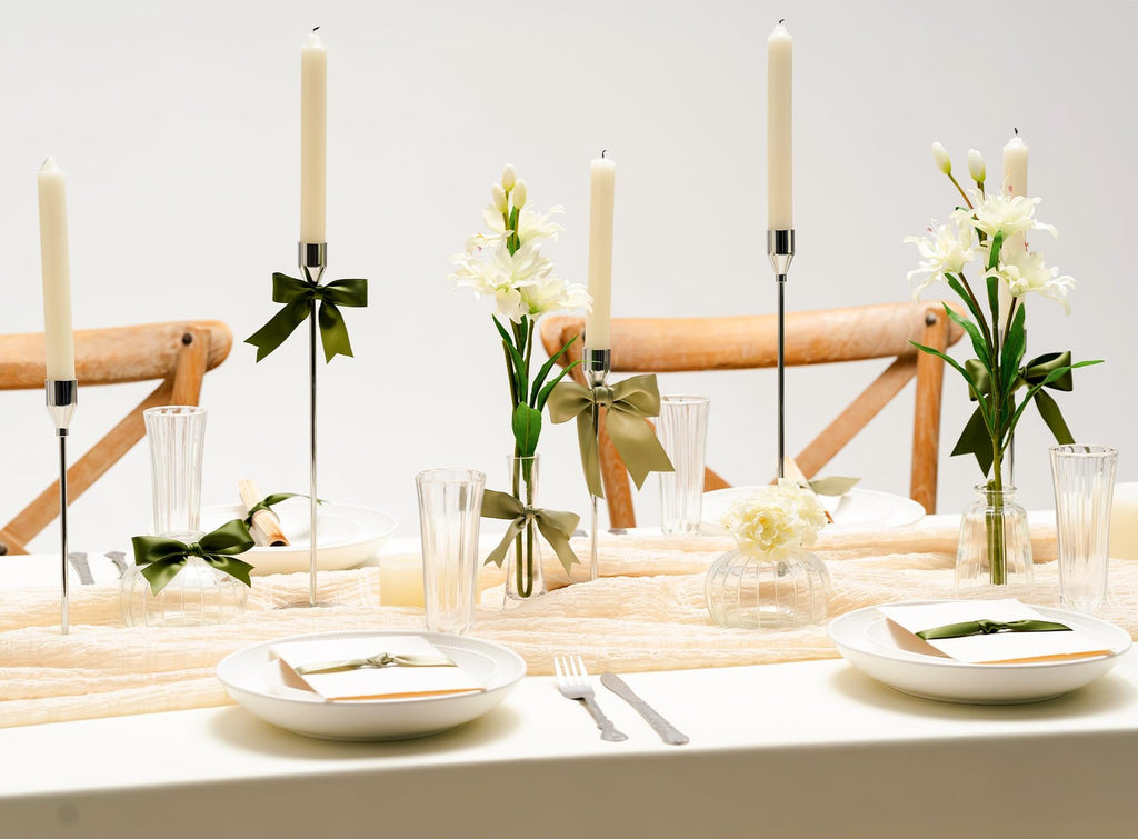 Table setting with candles, flowers, and plates decorated with green ribbon for a formal event.