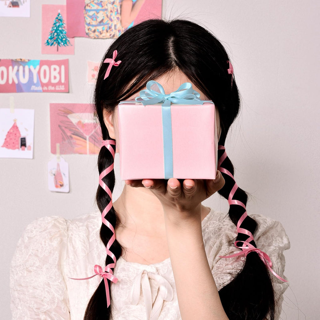 Person holding a pink gift box with a blue ribbon, with pink ribbons in their braided hair.