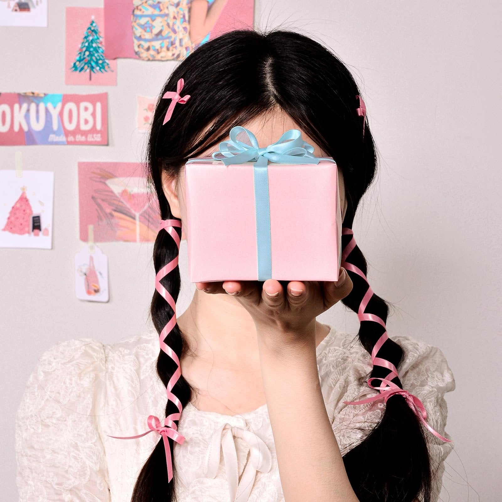 Person holding a pink gift box with a blue ribbon, with pink ribbons in their braided hair.