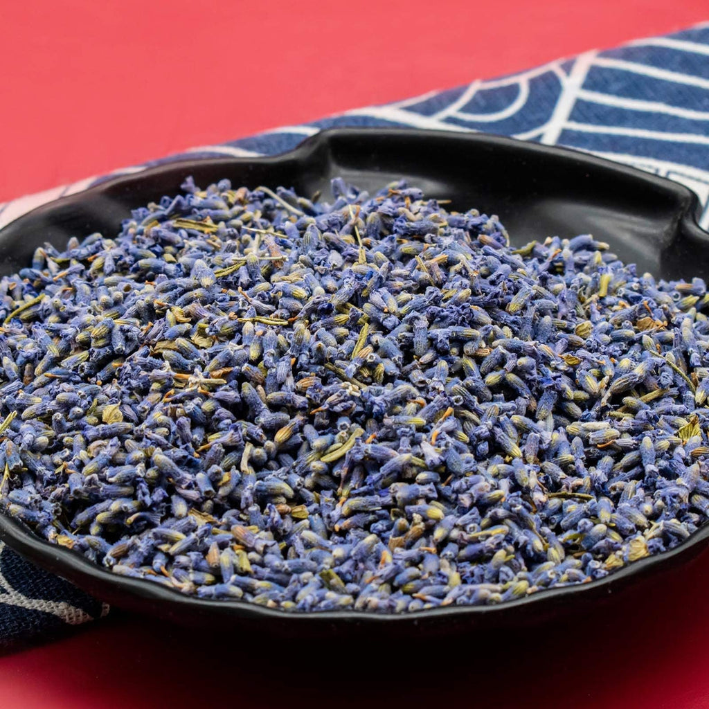 Close-up of dried lavender buds in a black bowl on a red background with a blue and white striped cloth.