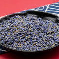 Close-up of dried lavender buds in a black bowl on a red background with a blue and white striped cloth.