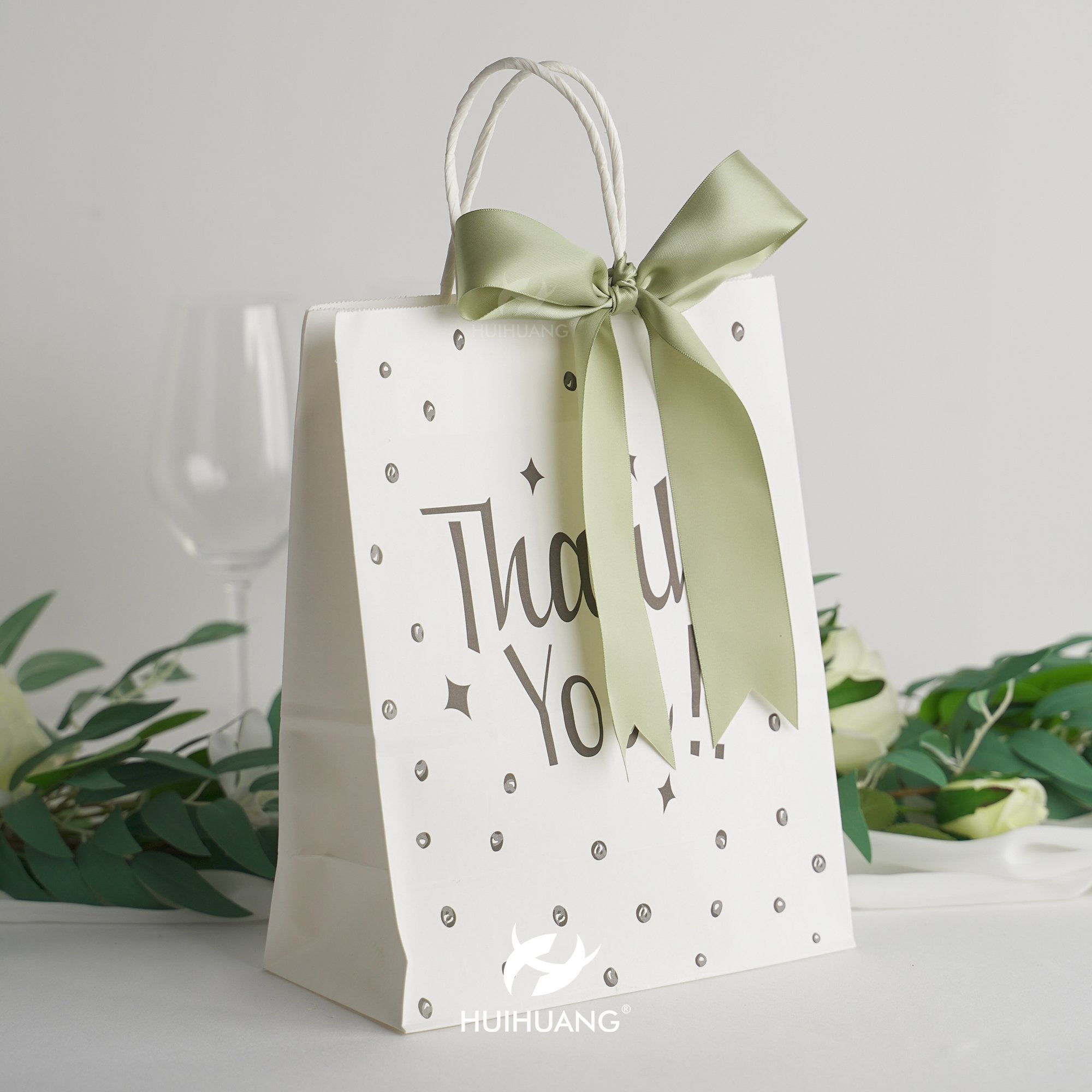 White gift bag with green ribbon bow and 'Thank You!' text, decorated with dots and stars.