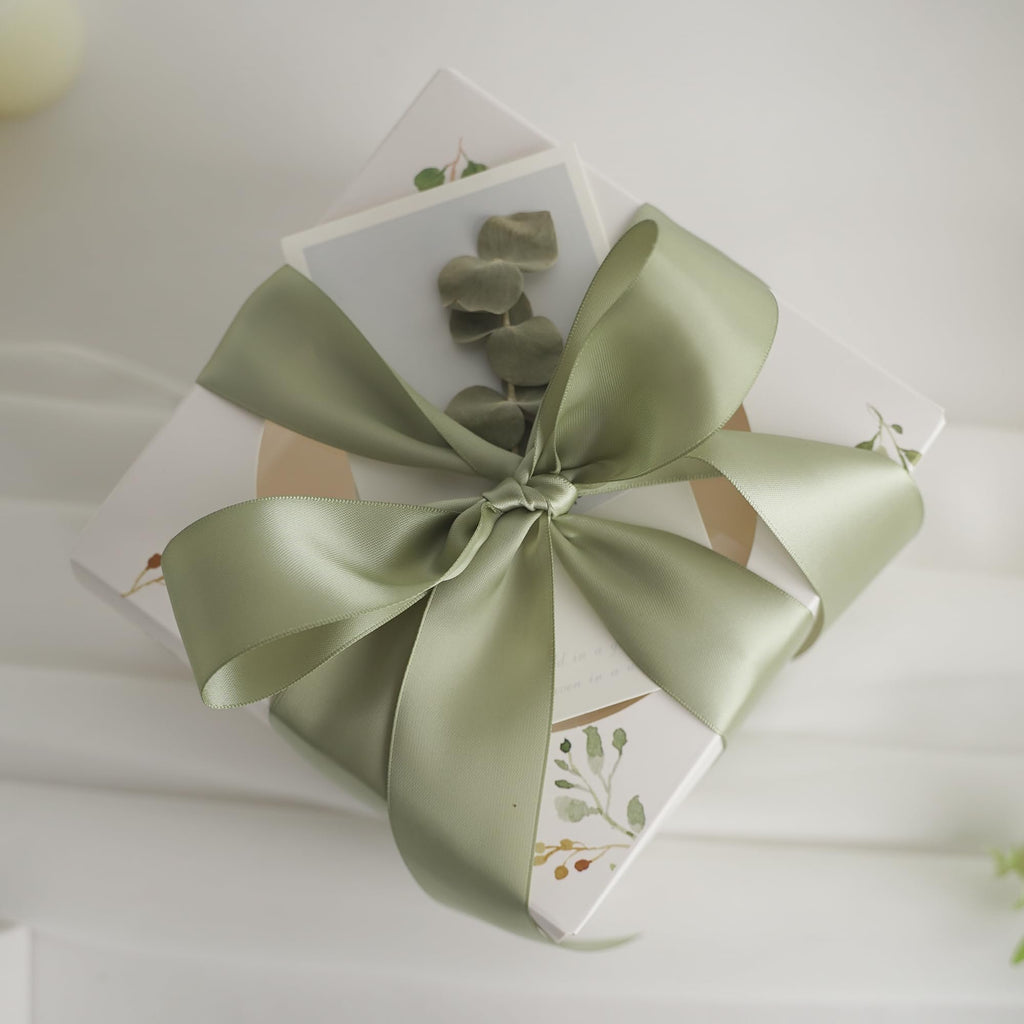 Dusty sage satin ribbon tied in a bow around a gift box with botanical illustrations.
