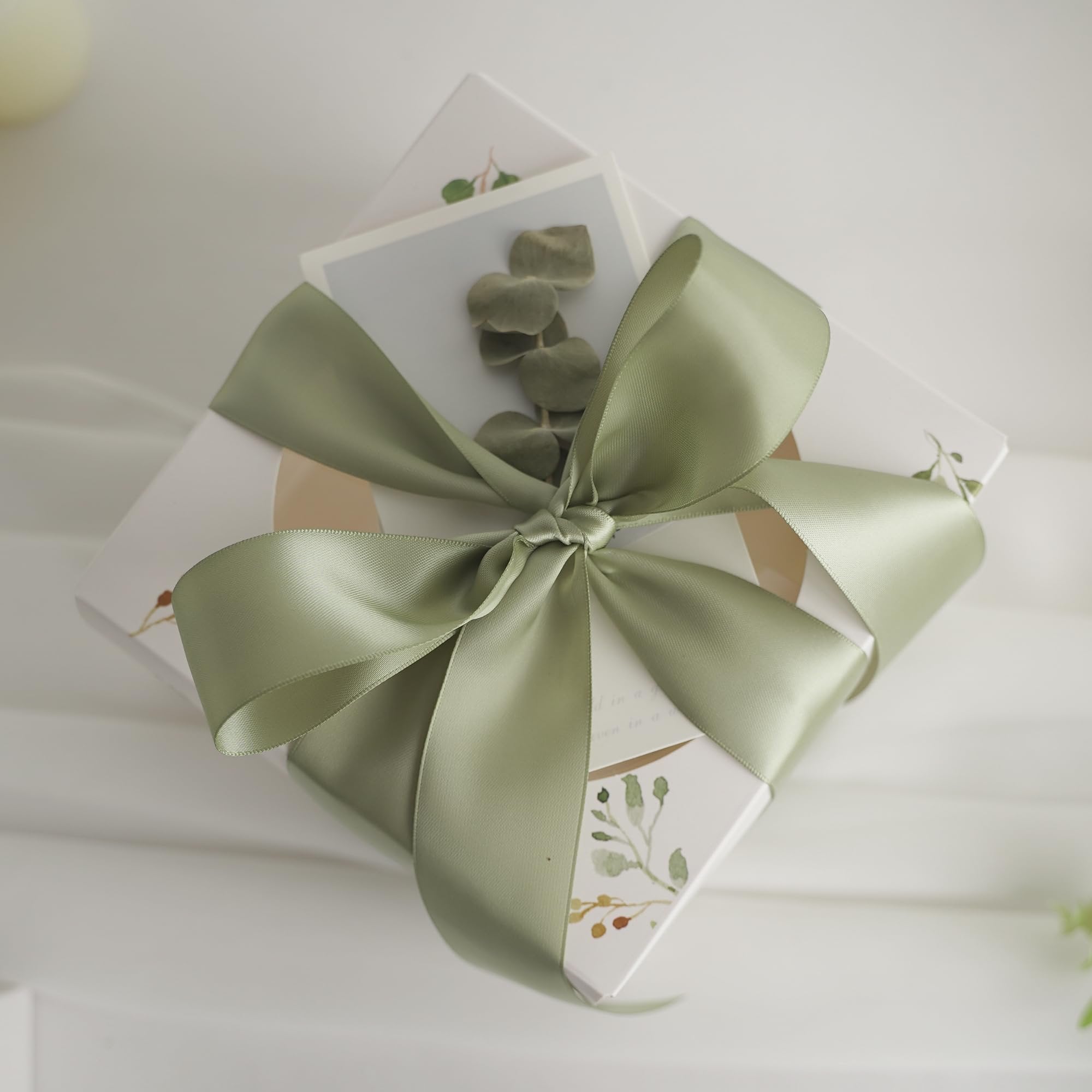 Dusty sage satin ribbon tied in a bow around a gift box with botanical illustrations.