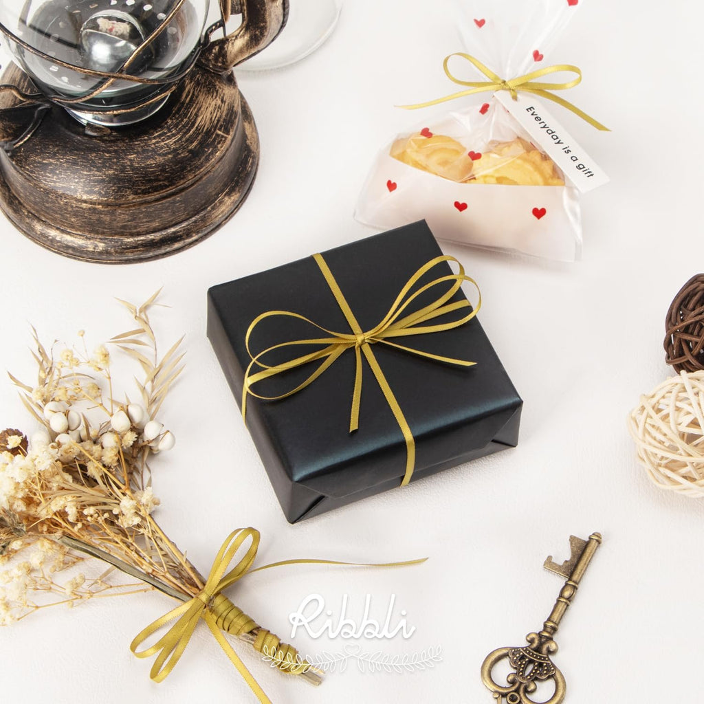 Black gift box with gold ribbon, dried flowers, and decorative key on white surface