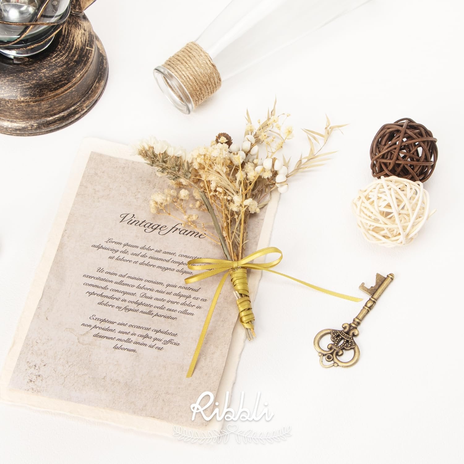 Flat lay of decorative items including a vintage frame, dried flowers, a key, and rattan balls on a white background.