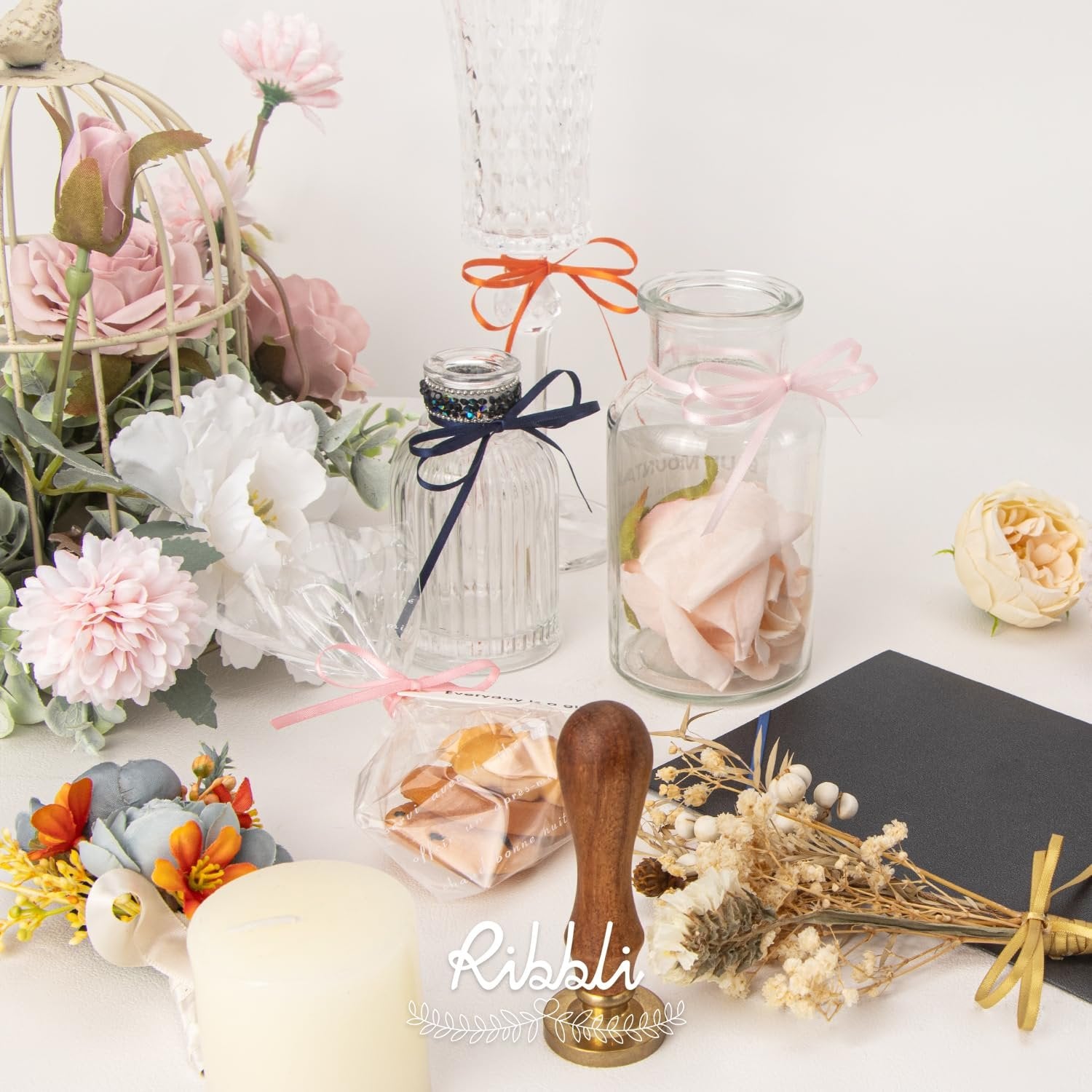 Brand name on a stamp next to decorative items including flowers, a candle, and glass jars.