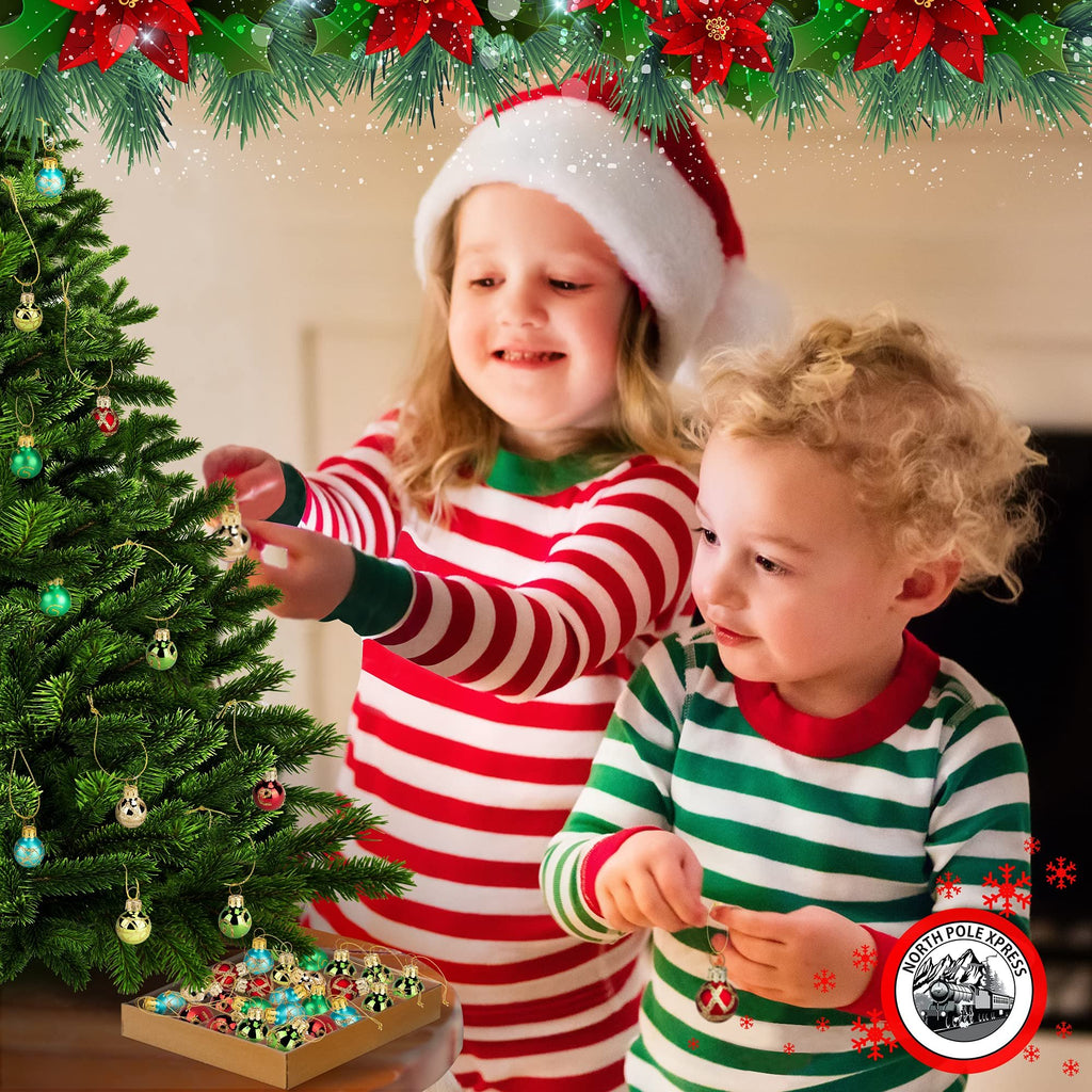 Two children in pajamas decorating a Christmas tree with mini ornaments, a box of ornaments is visible