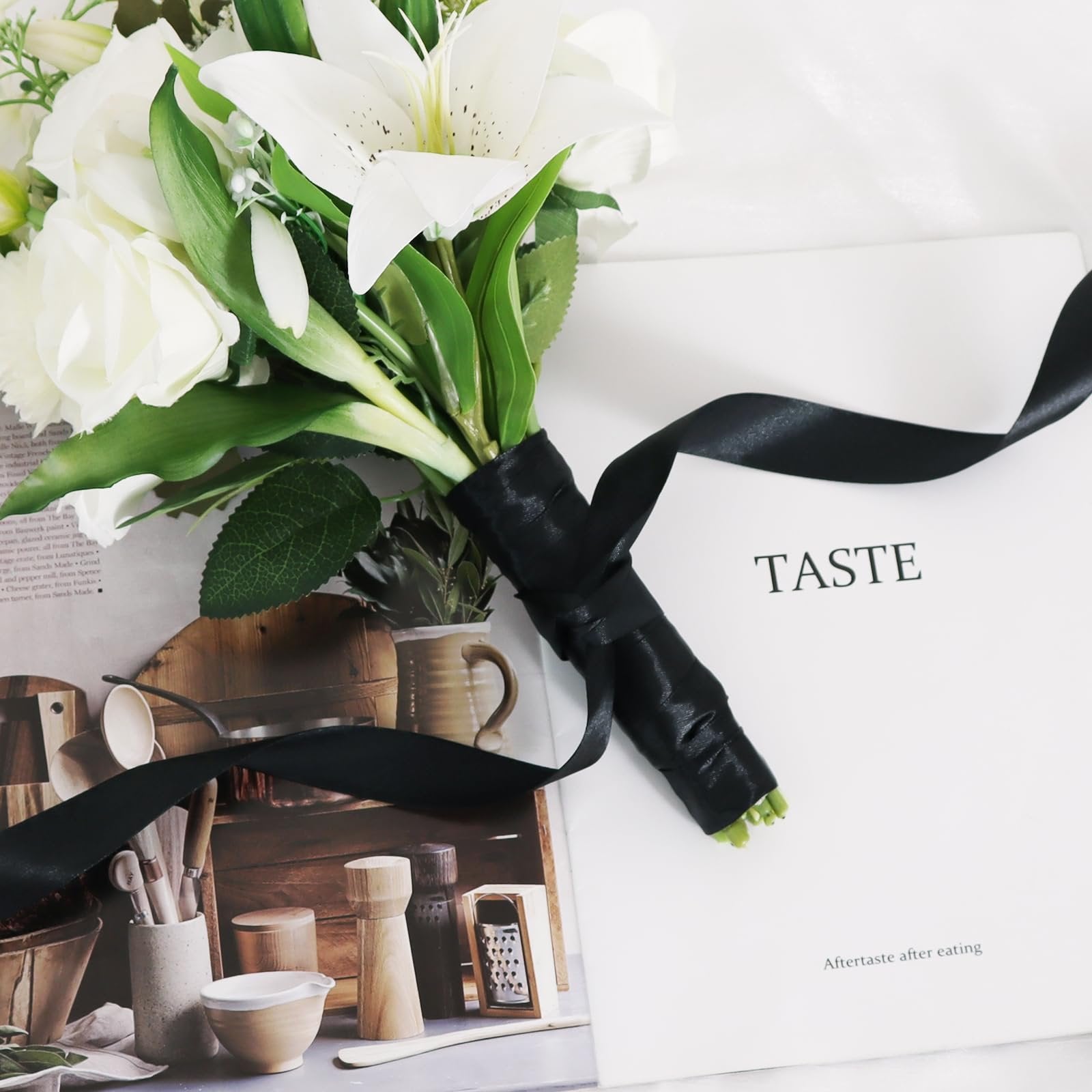 Close-up of a bouquet of white flowers with green leaves, tied with black satin ribbon, resting on a magazine with text.