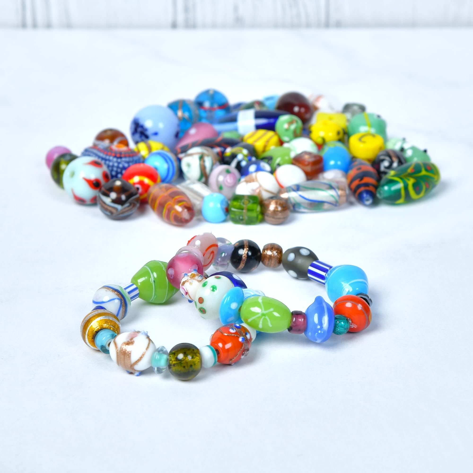 Assorted glass beads and two bracelets made from glass beads on a white surface