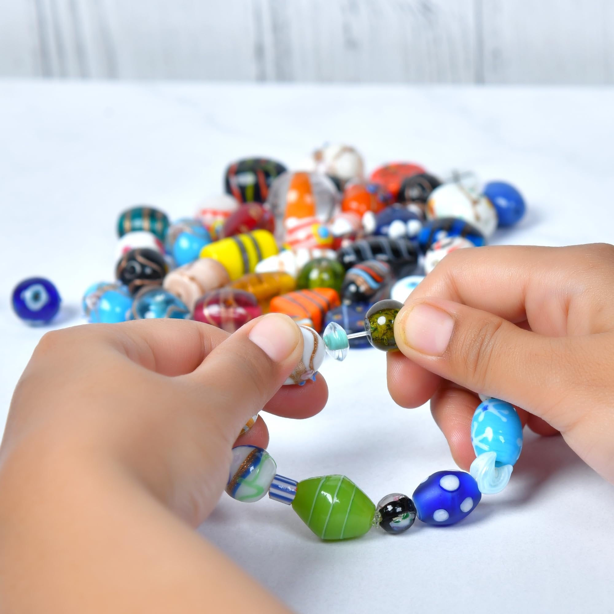 Hands stringing assorted glass beads to make a bracelet, with a pile of beads in the background.