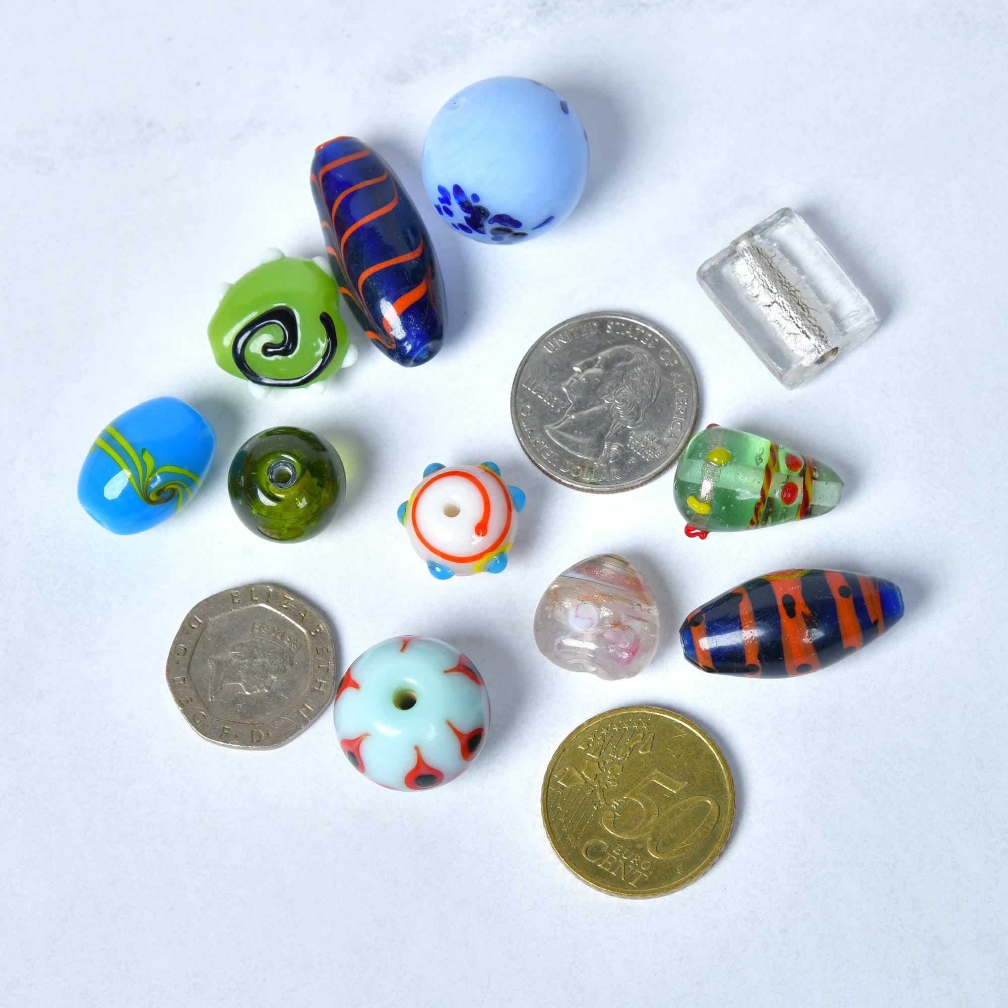 Assorted glass beads and coins on a white textured background, showing size comparison.