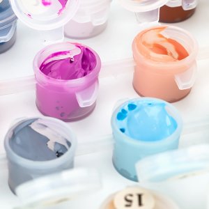 Close-up of paint pots with purple, orange, blue, and gray acrylic paints for a paint by numbers kit.