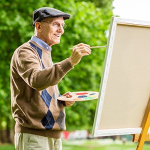 Elderly man painting outdoors on canvas with a palette and brush