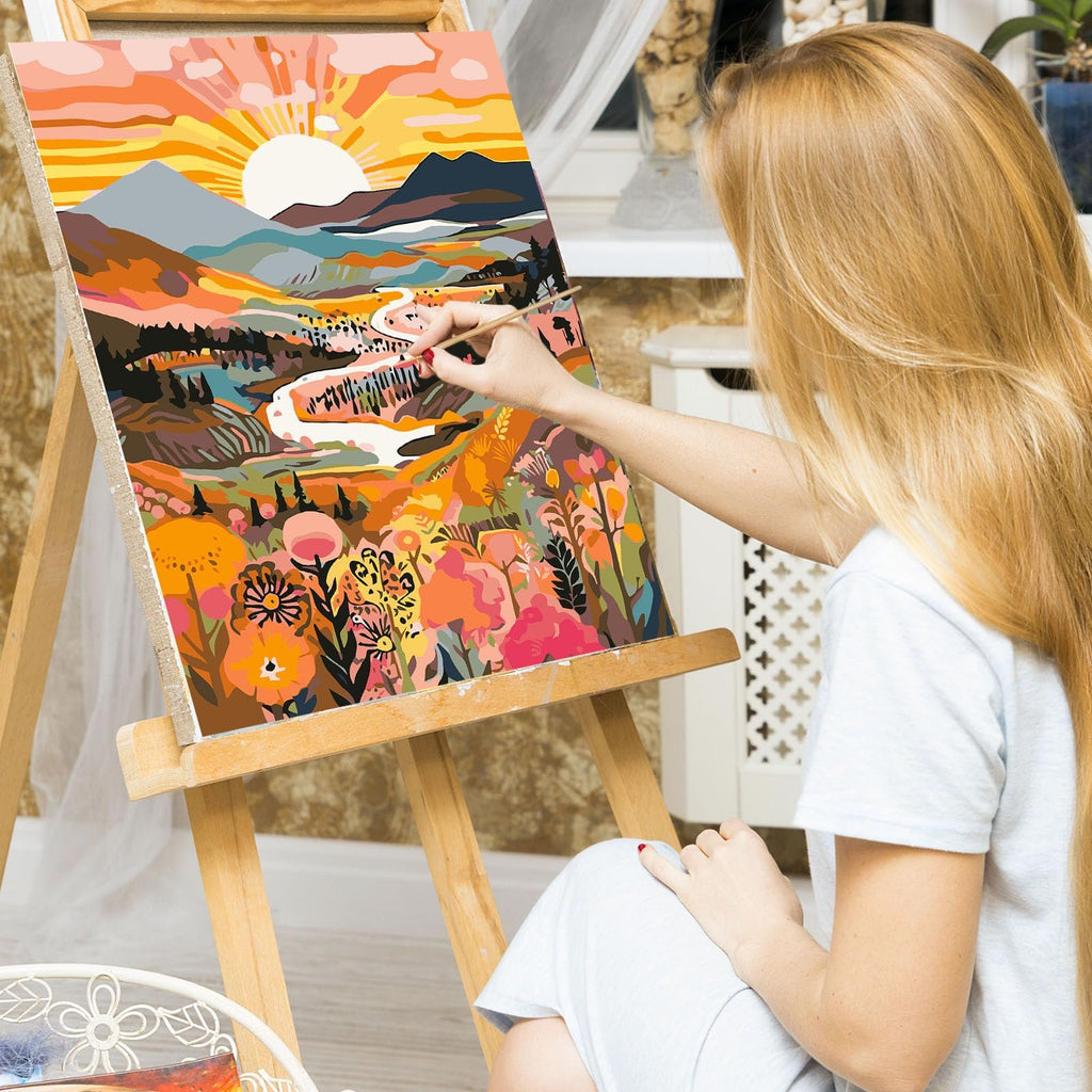 Woman painting a colorful landscape scene on canvas using a paint by numbers kit