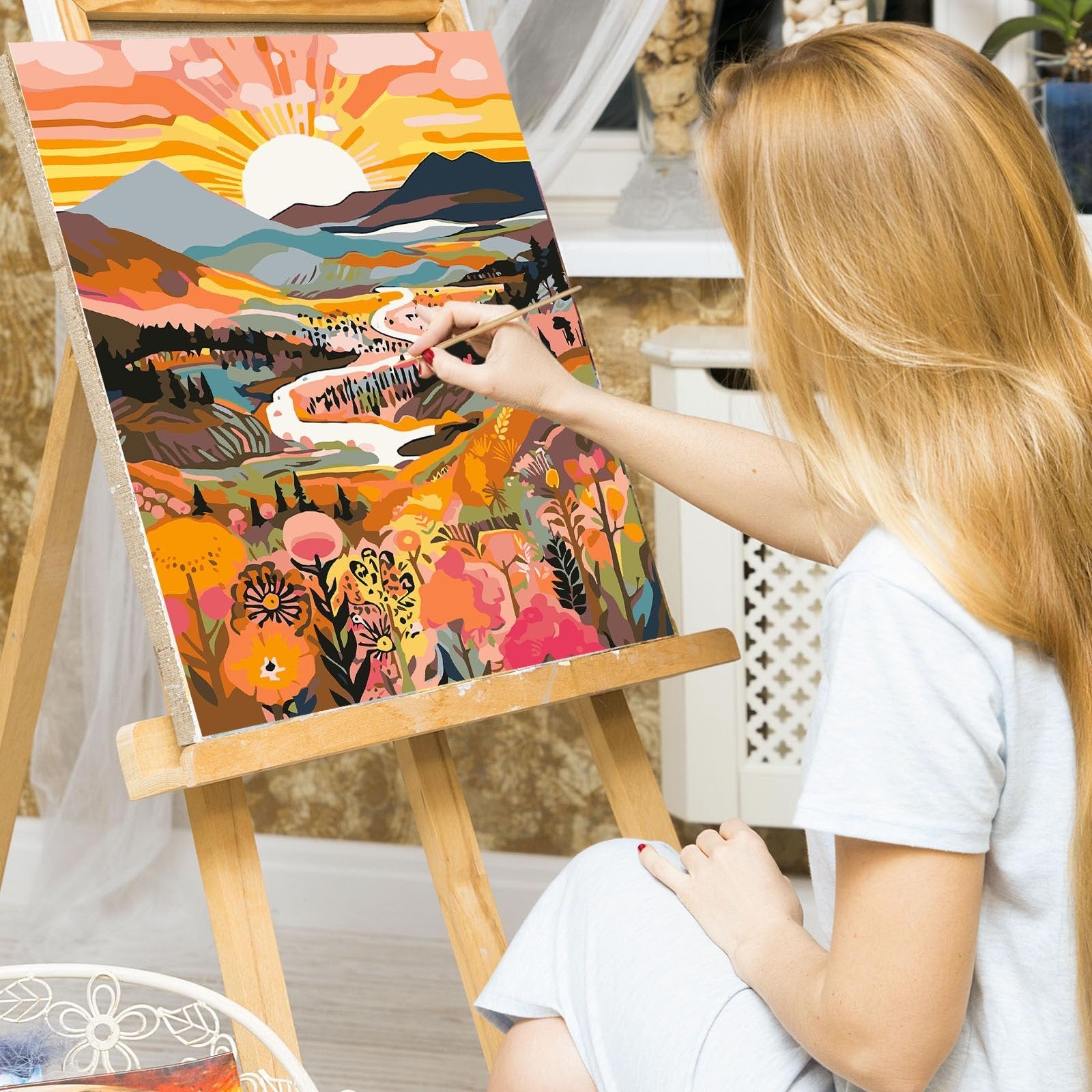 Woman painting a colorful landscape scene on canvas using a paint by numbers kit