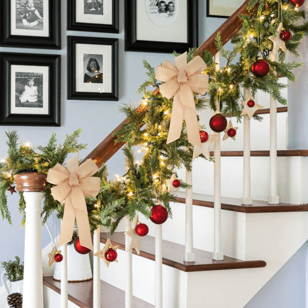 Two burlap bows decorating a Christmas garland on a staircase with framed photos on the wall.