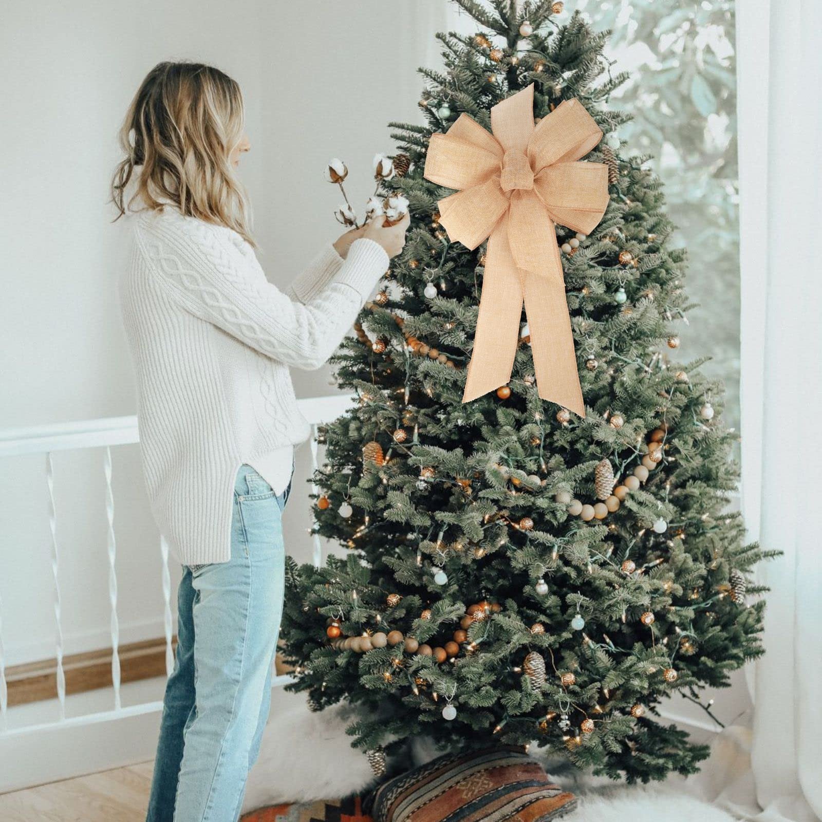 Woman decorating a Christmas tree with a large burlap bow and cotton stems.
