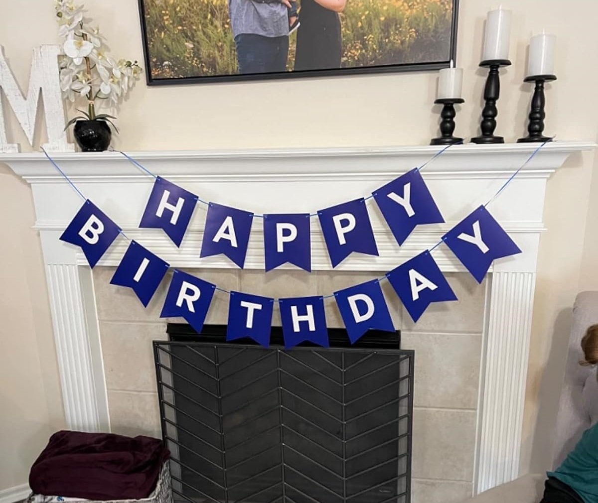 Blue and white 'Happy Birthday' banner strung across a fireplace mantel with decorative items.