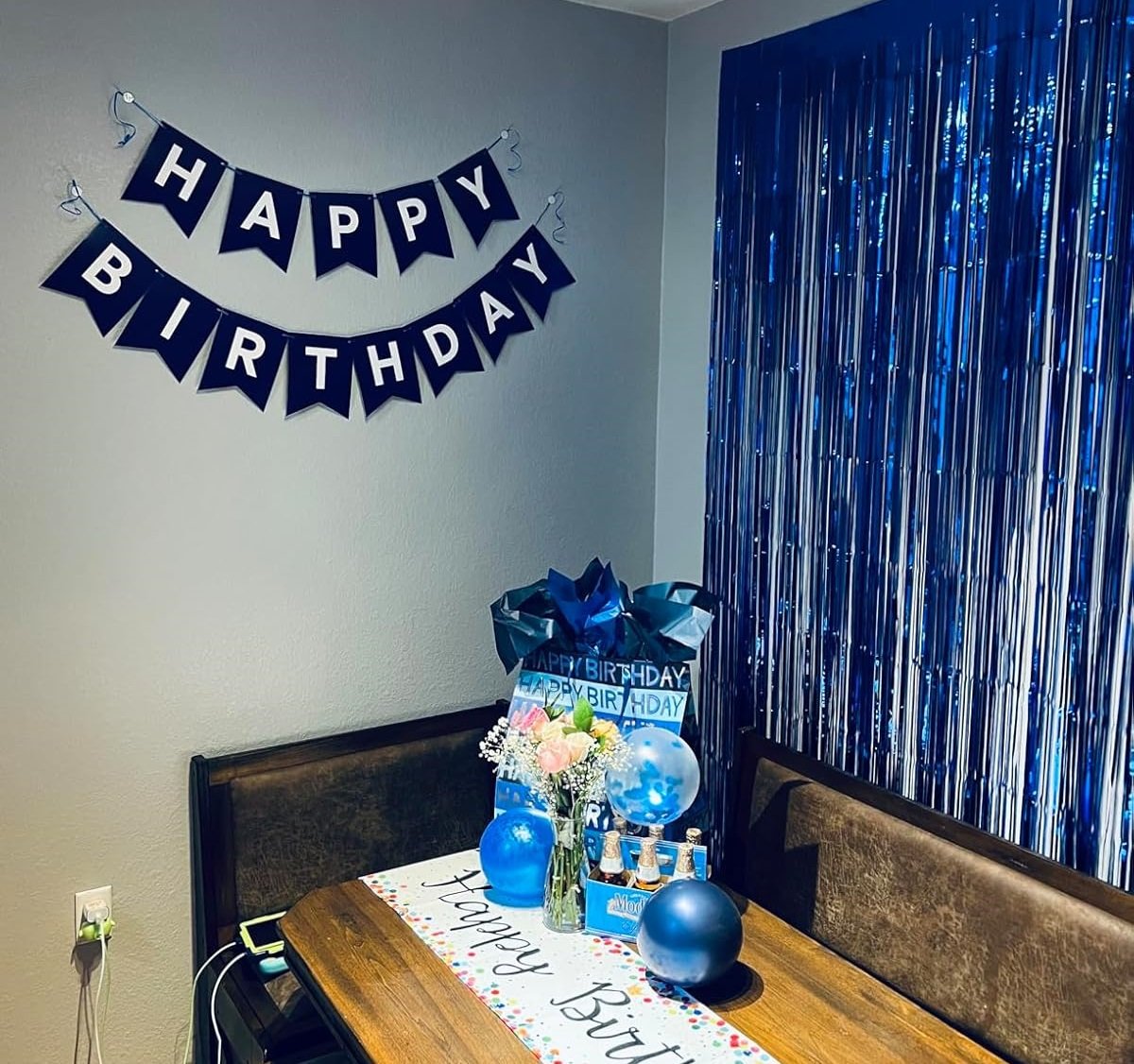 Party table setting with a navy blue 'Happy Birthday' banner hanging on the wall and blue metallic fringe curtains.