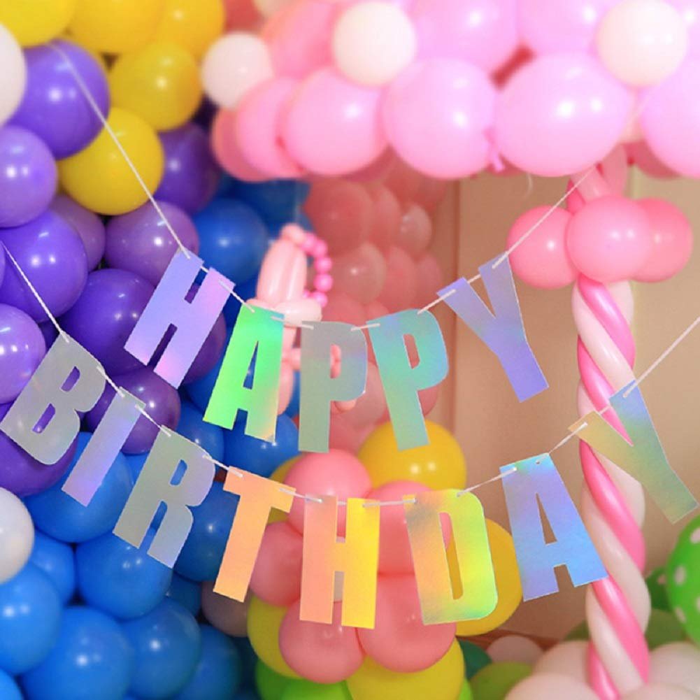 Holographic iridescent white 'Happy Birthday' banner strung with white cord, set against a backdrop of colorful balloons.