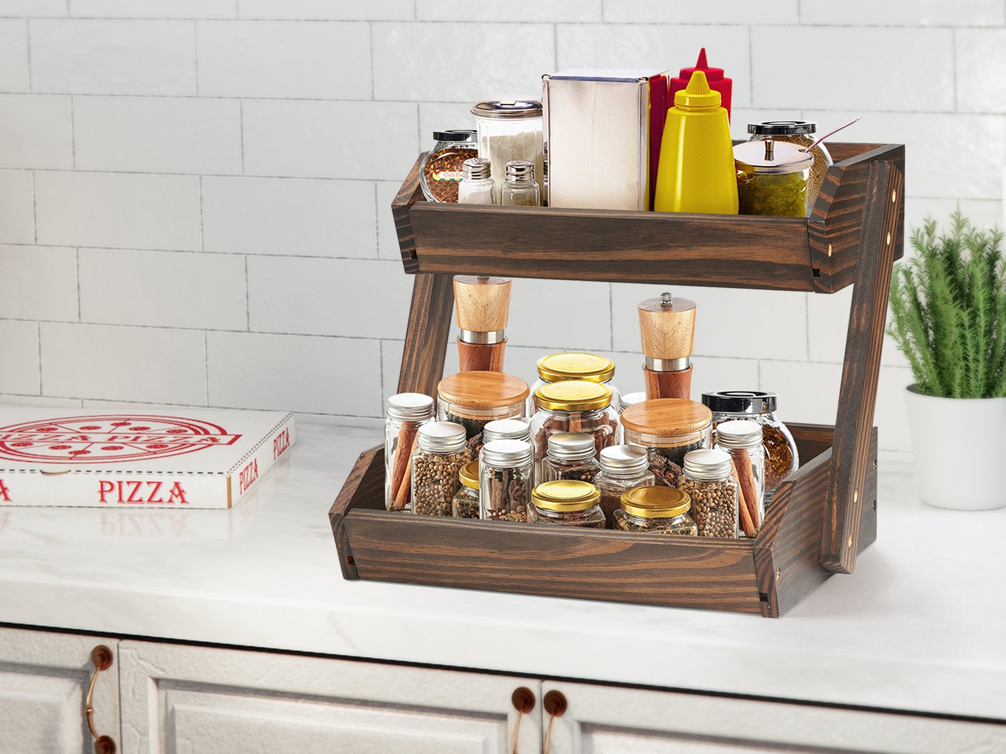 Two-tier wooden fruit basket filled with various jars of spices, condiments, and a napkin dispenser, on a kitchen counter next to a pizza box.