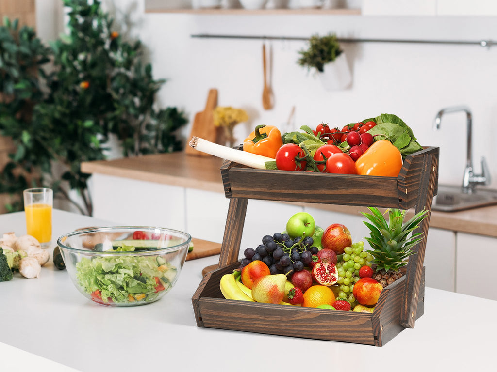 Two-tier wooden fruit basket filled with various fruits and vegetables on a kitchen counter.