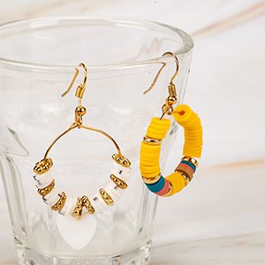 Two pairs of handmade hoop earrings with colorful clay beads and gold accents, displayed in a clear glass.
