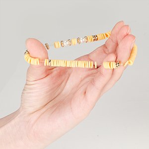 Hand holding a yellow clay bead bracelet with gold accents and clear elastic cord