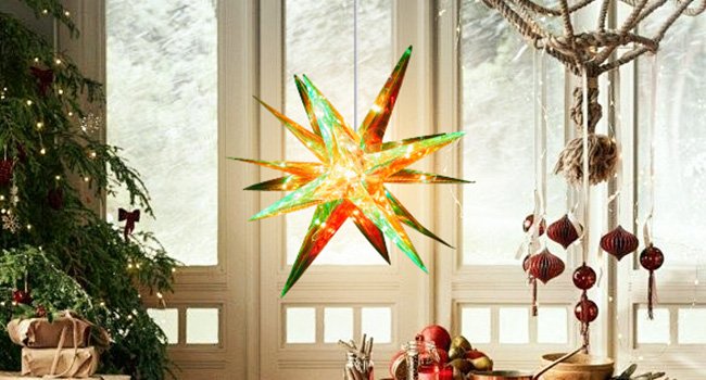 Illuminated multi-pointed star Christmas tree topper hanging indoors with a decorated Christmas tree and festive ornaments nearby.