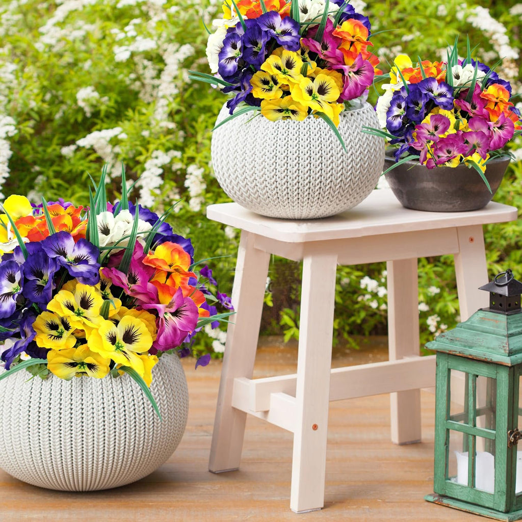 Three arrangements of colorful artificial pansy flowers in decorative pots on a wooden deck with a green lantern.