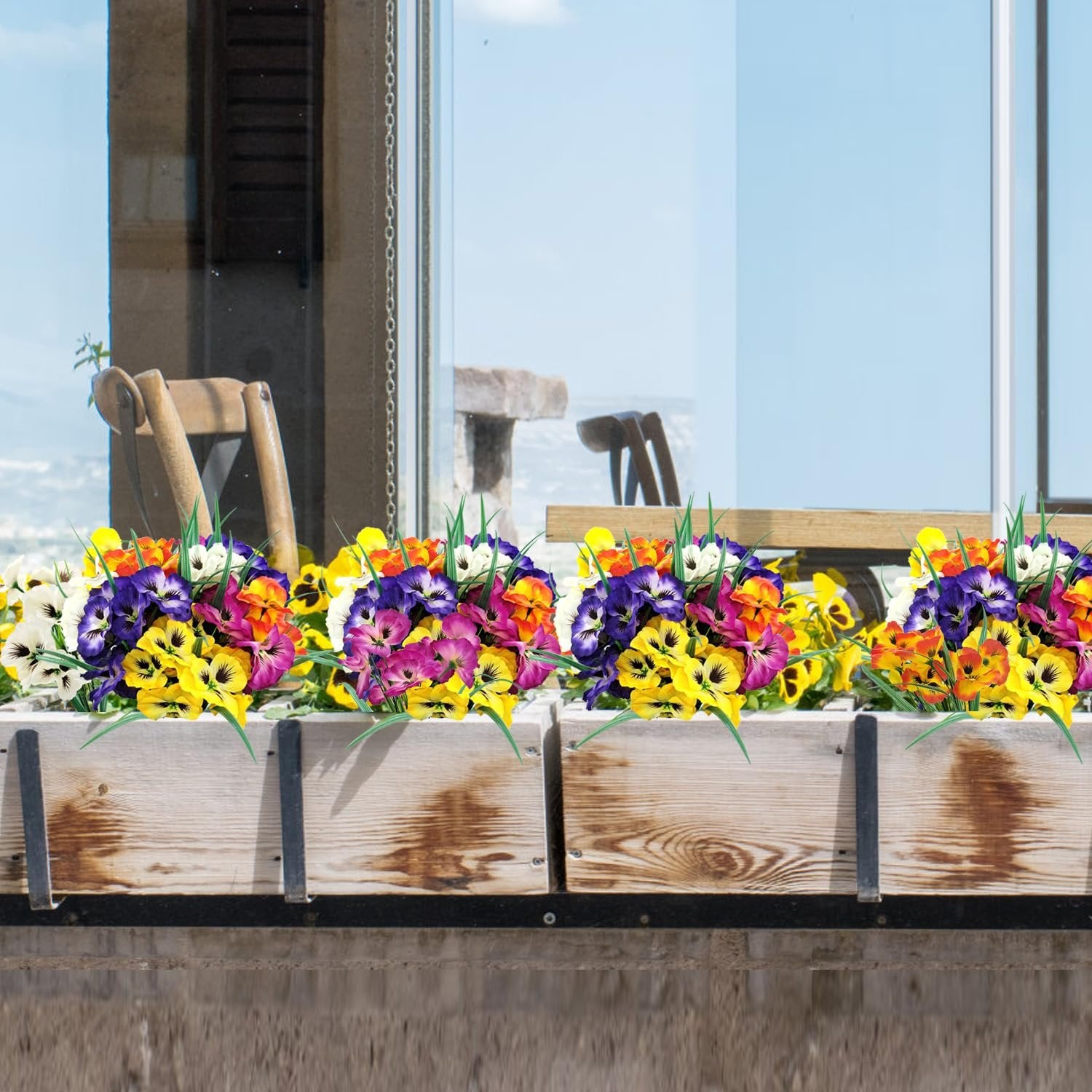 Artificial pansy flowers in multiple colors arranged in wooden planters on a windowsill.