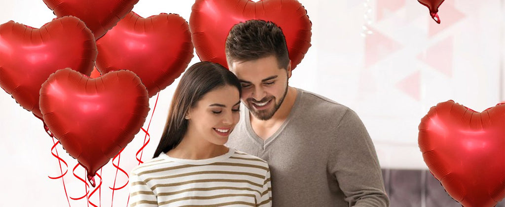 Couple smiling surrounded by red heart-shaped balloons with curling ribbons