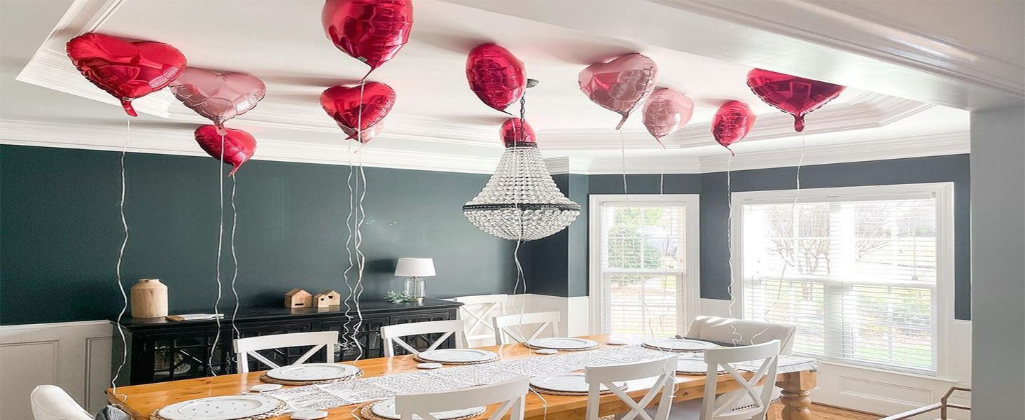 Heart-shaped foil balloons floating near a chandelier above a dining table set for a meal.