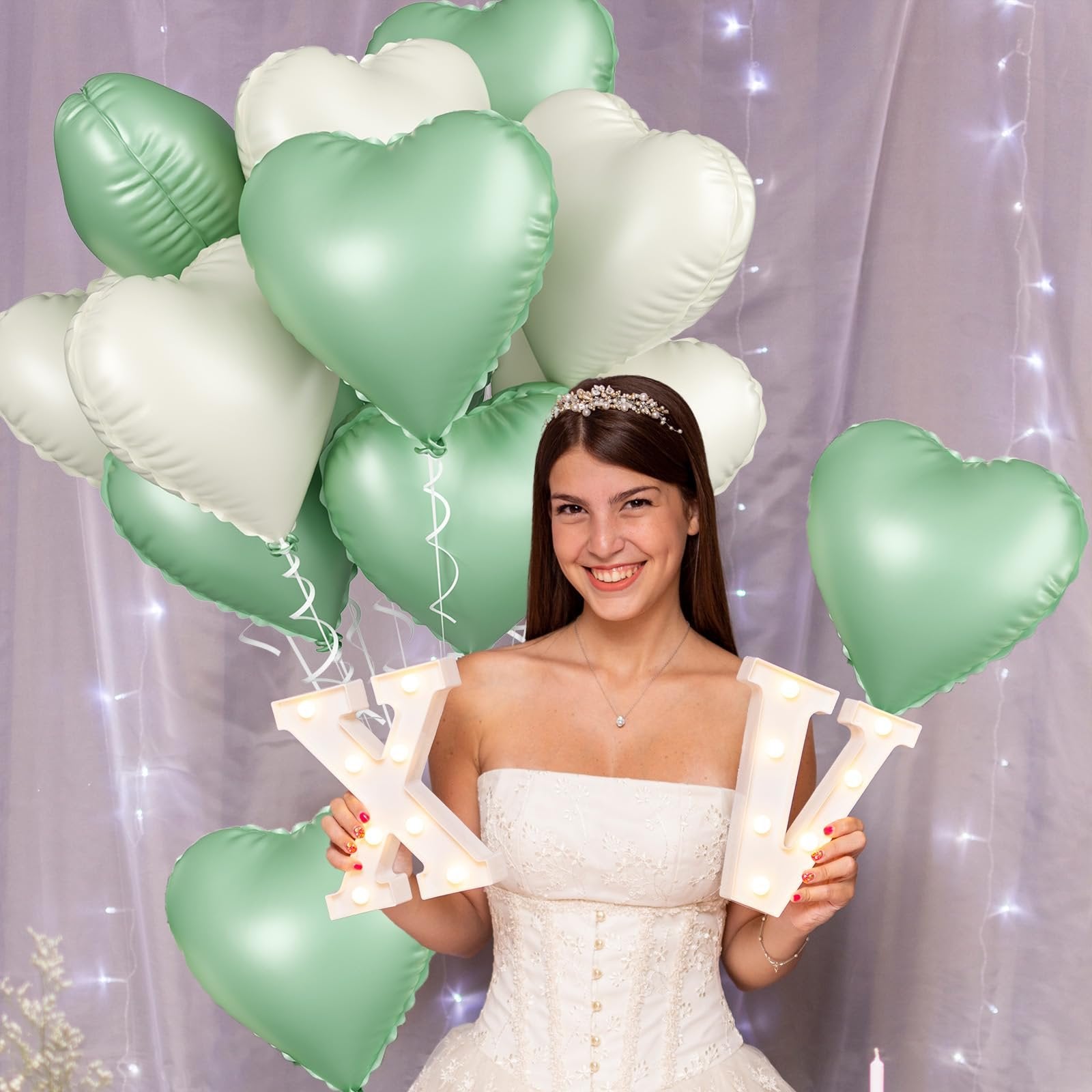 Woman in wedding dress holding illuminated letters 'XIV' with sage green and cream heart balloons