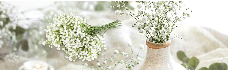 Two bouquets of white artificial baby's breath flowers, one in a vase and one lying down, with a candle and greenery.