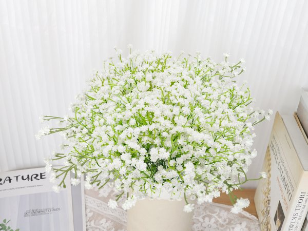 Bouquet of white artificial baby's breath flowers in a vase, with books and a magazine in the background.